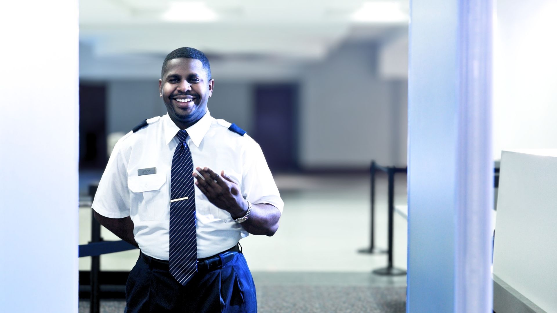 Friendly airport security officer in uniform welcoming a passenger to the private terminal screening area.